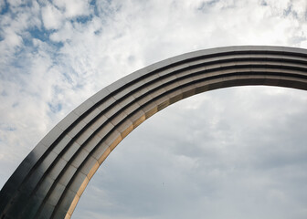 Obraz premium Looking up at metal arch in cloudy sky. High-tech titanium curve bridge made of lots of separate segments reflecting the warm sunlight.
