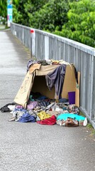 A makeshift shelter made of cardboard and clothing on a sidewalk.