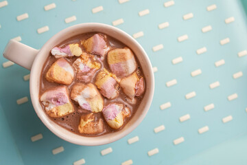 Hot cocoa with milk and pink marshmallows flat lay on blue background, minimal winter drink backdrop