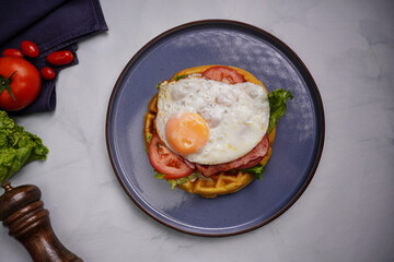 Fresh waffles with fried eggs, lettuce, tomatoes and served for breakfast on a flat table.