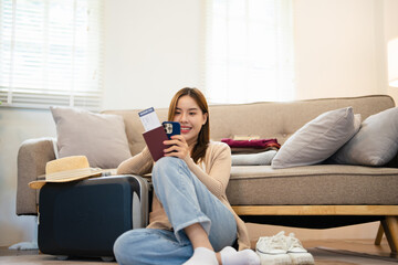 Asian woman uses her mobile phone to checking travel information, plan a trip while packing things...