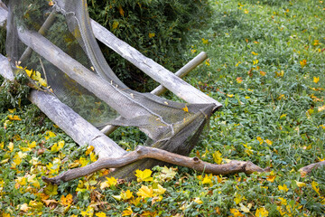 Old weathered wooden frame with netting. The frame is placed on the ground and is covered with cobwebs. There are lots of fallen leaves around the frame, indicating the autumn season.