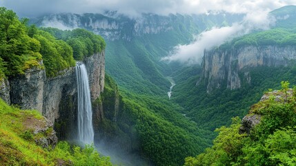 Fototapeta premium Waterfall cascading into a lush green valley with misty mountains.