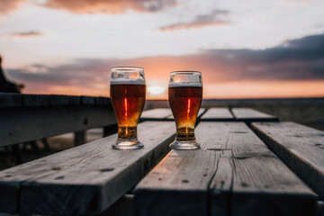 two glasses of beer sit on a wooden table