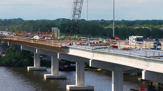 Hardhat workers at highway bridge construction in Ellenton, Florida. Development of Trooper J.D. Young Memorial Bridge crossing the Manatee River. American freeway road with moving traffic cars.