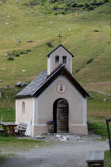 Fototapeta premium Small mountain chapel surrounded by green meadows under a blue summer sky, ideal for hiking and tourism.