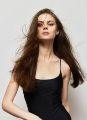 Naklejka premium Elegant young woman with long flowing hair poses confidently in minimalistic black outfit against a neutral backdrop. Fashion and beauty concept.