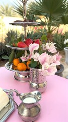 Fruits displayed on tiered stand with smooth creamy dessert, polished silver tray and delicate flower in silver vase adding charm to balanced fruits and dessert presentation. Luxurious table concept.