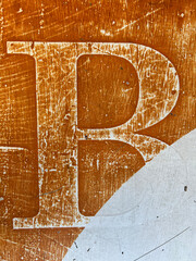 The Letter B worn, faded and weathered on an orange table 