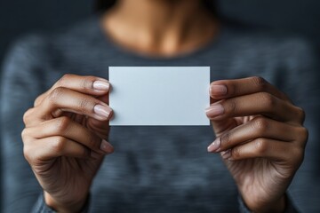 Fototapeta premium Person holding a blank card with both hands against a dark background in a well-lit environment