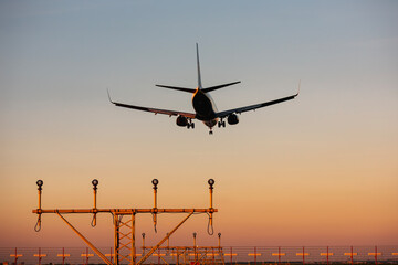 Silhouette of airplane landing at airport at beuatiful summer sunset. Plane above navigation light...