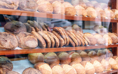 Freshly baked loaves and rolls are neatly arranged on wooden shelves in a bakery window, creating a tempting display