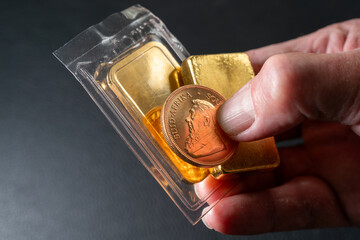 Closeup of hand holding two bullions and a Krugerrand coin on top. Symbol of wealth and financial freedom.