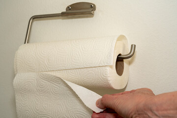 Hand is ripping off a wipe from a kitchen roll, attached to the wall. White background, white space.