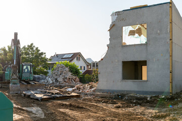 Half torn down demolition house under a blue sky. A pile of rubbish lying around. Excavator...