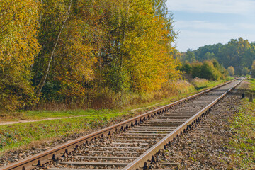 Obraz premium Railway tracks running through a scenic autumn landscape, surrounded by trees with vibrant yellow and green foliage