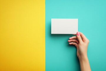 Fototapeta premium Hand holding a blank card against a vibrant turquoise and yellow background