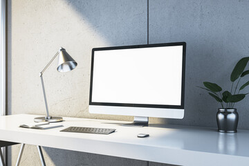 Modern desk with computer monitor, lamp, and plant on clean white table in office interior with concrete wall. 3D Rendering