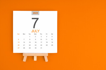 Calendar page for July 2025 with wood easel on orange background.