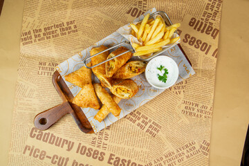 Samosas and crispy fries served on a wooden board