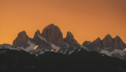 Golden sunrise illuminating distant mountain peaks, creating layered silhouettes of the Dolomites against a warm orange sky.