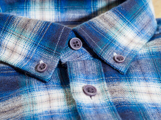 Close-up of a blue plaid shirt collar with button details in soft lighting.