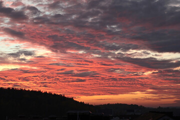 Fototapeta premium Orange, red sunset over forest and village. Romantic dramatic background for design. Sky and clouds. 