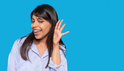 Young woman playfully listening with a smile against a bright blue background