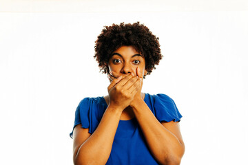 Surprised young african woman covering mouth with hands and staring at camera while standing over white background