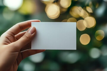 Blank business card held in hand with blurred lights in the background during a cozy evening