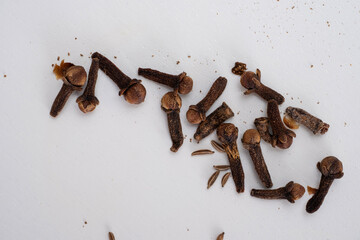 A close up of dried cloves and caraway seeds scattered on a white background. The spices showcase their natural textures and rich colors, often used in cooking, baking, and herbal remedies.