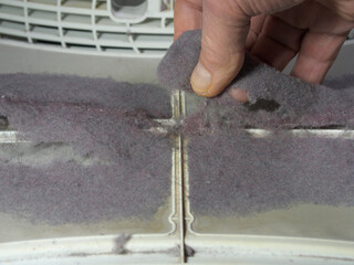 Closeup of a man’s hand removing the build-up of garment lint fluff from the filter of a tumble dryer.