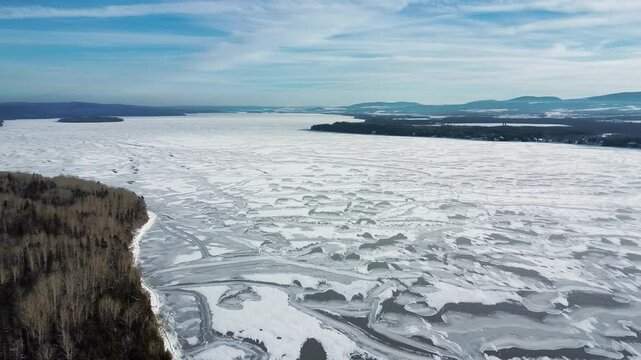 Panoramic drone view of Lake Matapedia frozen solid during winter, revealing intricate ice textures shaped by northern cold and surrounded by dense boreal forest in Quebec, Canada.