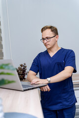 Medic on laptop in office. A young healthcare worker in scrubs is focused on his laptop in a modern...