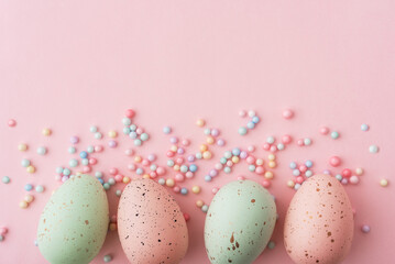 Colorful speckled eggs arranged on a pink background with small candy decorations for seasonal celebrations