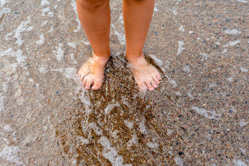 Bare feet standing in shallow water on a sandy beach with natural textures.

