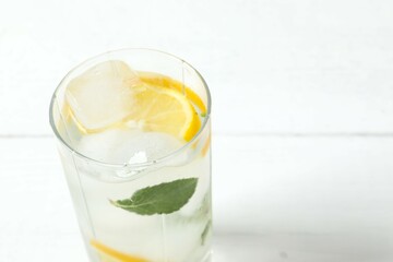 Summer refreshing lemonade drink or alcoholic cocktail with ice, mint and lemon slices on the table. Fresh healthy cold lemon beverage. Water with lemon