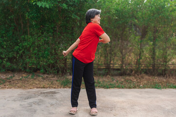 Happy asian old woman stretching arms and body at park in morning after exercise, wear red t-shirt, healthy routine.