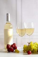 Bottle of white wine with grapes and glasses on table