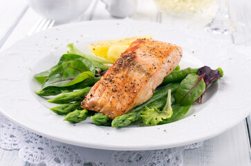 Traditional fried salmon fillet with green asparagus, boiled potatoes and green salad served as close-up on a classic design plate