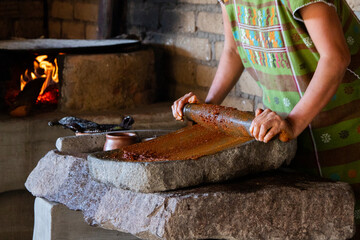 Woman from an indigenous community in Oaxaca preparing traditional red mole with a metate, a tool for grinding ingredients in Mexico.