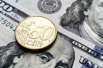 Close-up of a 50 euro cent coin on US 100 dollar bills in focus.