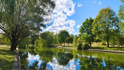 The banks of the river are concreted. Willows grow on the grass, their branches overhanging the...