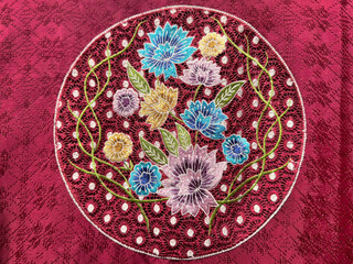 Close up of custom made flower and leaves ornamental medallion sewn on a red fabric. Custom floral medallion pattern knitted and sewn on Chinese red cloth seamless texture.