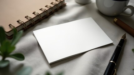 Blank business cards rest on a textured surface beside an elegant fountain pen and a spiral notebook