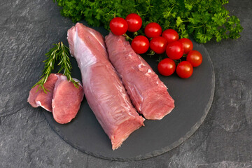 Fresh pork loin with tomatoes on a slate plate.