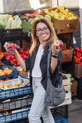 A woman in her 30s-40s selects fresh grapes at an outdoor market. The photo highlights organic produce, healthy eating, vegan lifestyle, sustainable living, and mindful nutrition choices