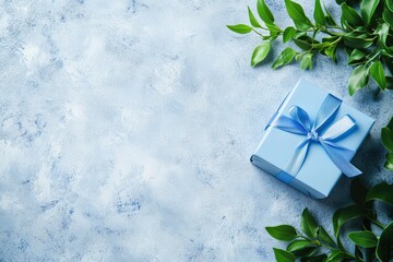 Elegant blue gift box with ribbon and green leaves on textured background