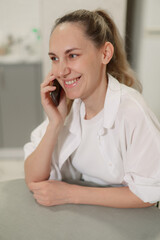 Fototapeta premium Happy young smiles woman chatting on the phone while lounging on a couch in her living room