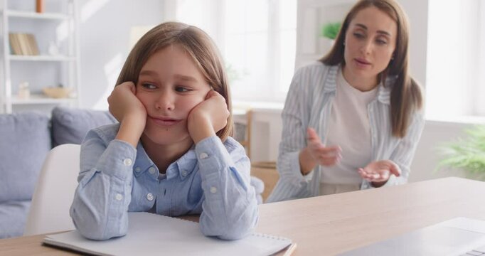 Frustrated mother emotionally scolding her preteen child, expressing her anger and disappointment. Preteen son sitting at desk, avoiding eye contact, refusing to discuss school or emotional problems.